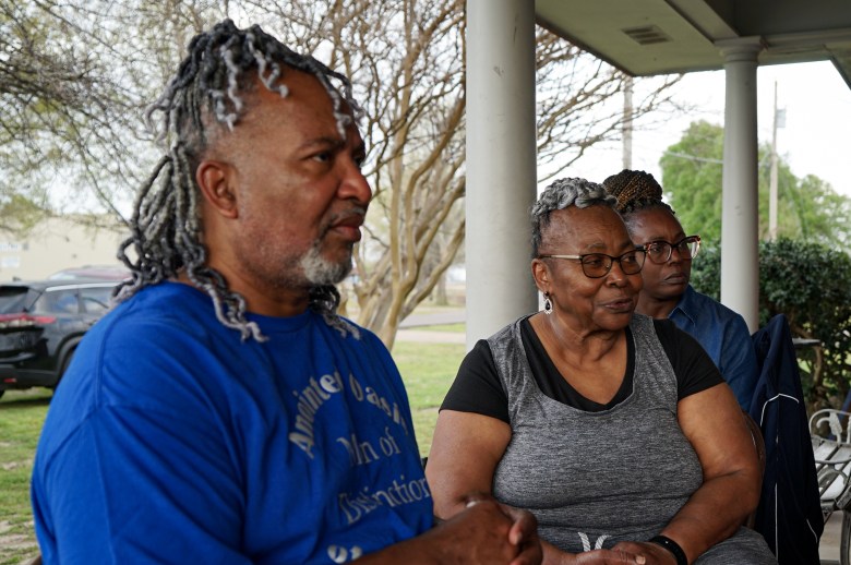 A middle-aged man sits beside his mother and another woman on a house porch.